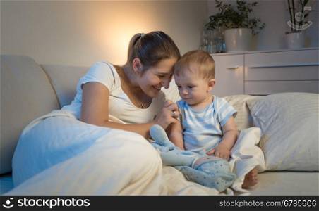Portrait of beautiful smiling mother lying on bed and playing with her baby before going to sleep
