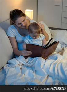 Portrait of beautiful smiling mother reading story to her baby boy before going to sleep