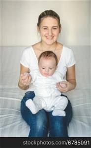 Portrait of beautiful smiling mother sitting on bed and holding her baby boy