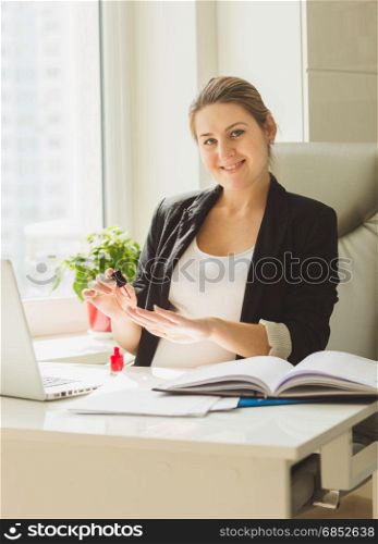 Portrait of beautiful smiling secretary painting nails at office