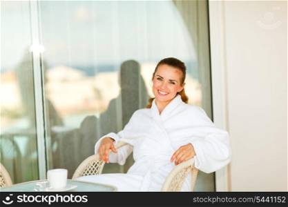 Portrait of beautiful smiling woman in bathrobe sitting at table on terrace