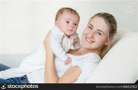Portrait of beautiful smiling woman lying with her cute baby on pillow at bed