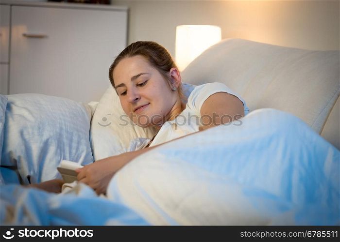 Portrait of beautiful smiling woman reading on digital tablet at bed before sleeping