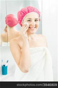 Portrait of beautiful smiling woman using face cream after having shower