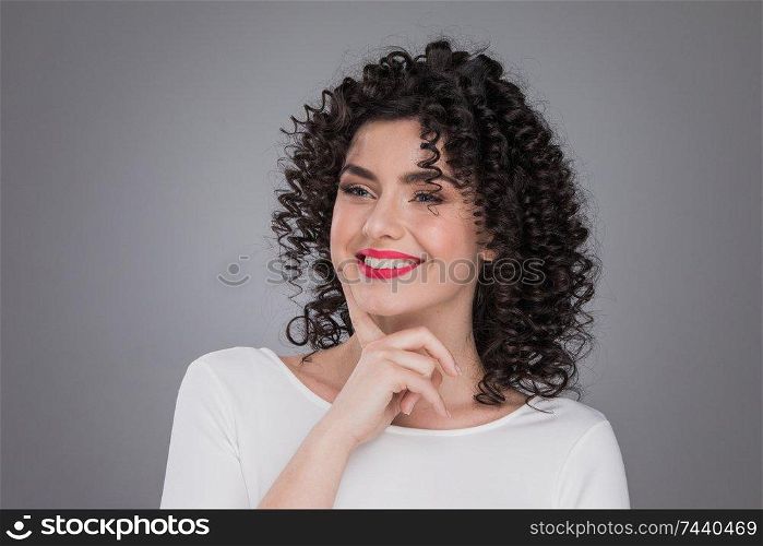 Portrait of beautiful smiling woman with curly hair, gray background. Beautiful woman with curly hair