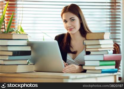 Portrait of beautiful student girl sitting among the books and working on a laptop