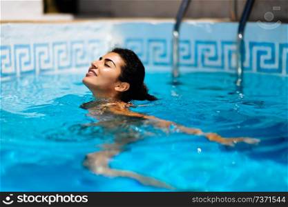 Portrait of beautiful tanned woman in bikini relaxing in swimming pool spa. Hot summer day and bright sunny light. . Beautiful tanned woman in bikini relaxing in swimming pool