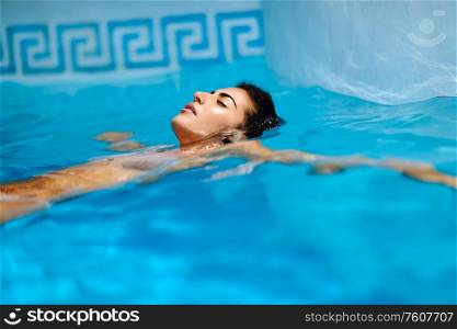 Portrait of beautiful tanned woman in bikini relaxing in swimming pool spa. Hot summer day and bright sunny light.. Beautiful tanned woman in bikini relaxing in swimming pool