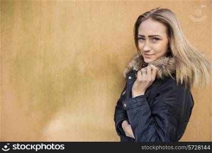 Portrait of beautiful teenage girl in jacket standing against wall