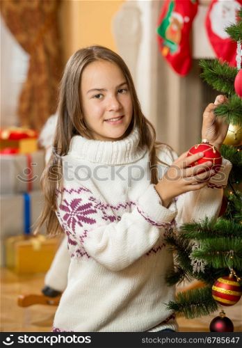 Portrait of beautiful teenage girl posing at Christmas tree with red bauble