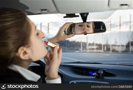 Portrait of beautiful woman applying lipstick in car