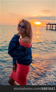 Portrait of beautiful woman at sunset on the beach. Outdoor fashion portrait of stylish girl wearing jeans jacket on the beach.