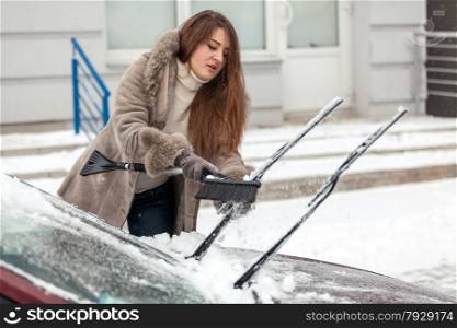 Portrait of beautiful woman cleaning car with brush after blizzard