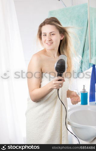 Portrait of beautiful woman drying long hair at mirror