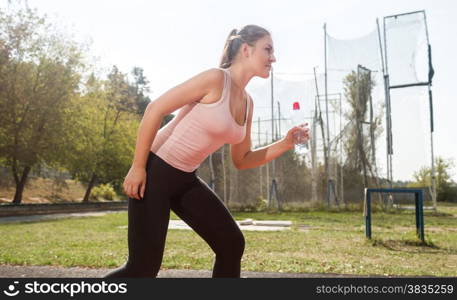 Portrait of beautiful woman holding bottle of water running on stadium