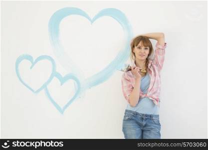 Portrait of beautiful woman holding paint brush with hearts painted on wall