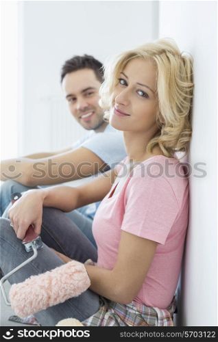 Portrait of beautiful woman holding paint roller with man in background