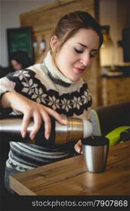 Portrait of beautiful woman in sweater pouring coffee from thermos in cup