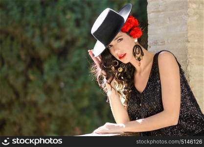 Portrait of beautiful woman, model of fashion, wearing spanish hat and red carnations in her hair