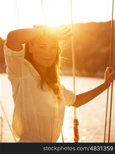 Portrait of beautiful woman on yacht deck in warm yellow sunset light, attractive model posing on sailboat, luxury cruise on the sea, summer vacation concept