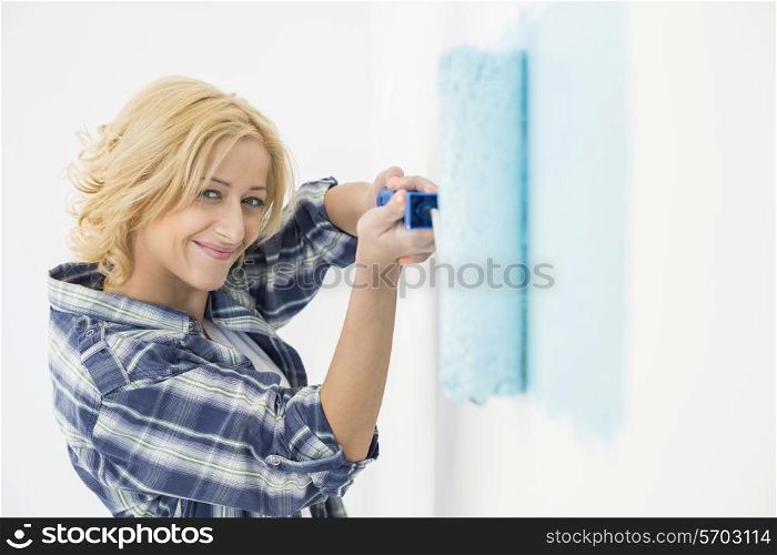 Portrait of beautiful woman painting wall with paint roller
