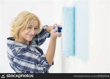 Portrait of beautiful woman painting wall with paint roller