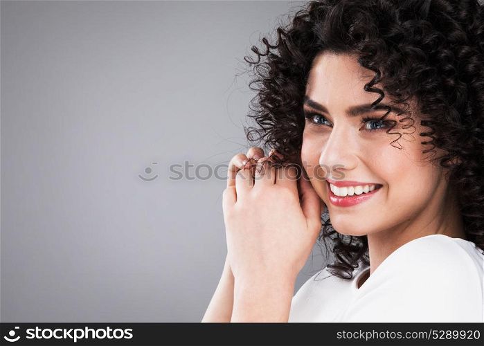 Portrait of beautiful woman. Portrait of amazing beautiful smiling woman with curly hair on gray background with copy space