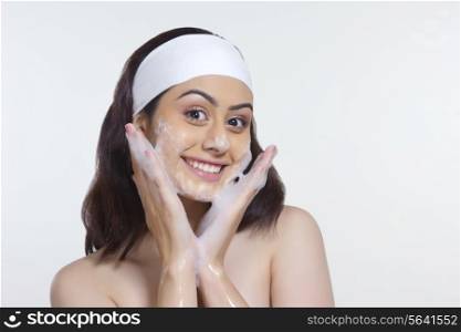 Portrait of beautiful woman scrubbing face with soap against white background