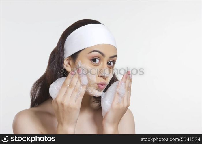 Portrait of beautiful woman scrubbing face with soap sud against white background