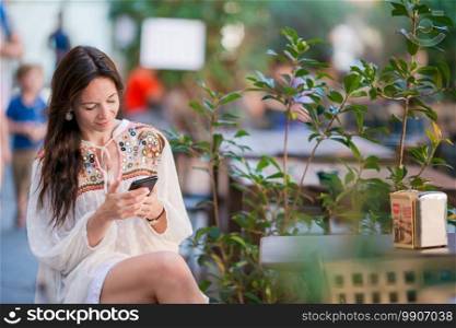 Portrait of beautiful woman sitting in outdoor cafe drinking coffee and using smartphone. Young girl looking on display.. Portrait of beautiful woman sitting in outdoor cafe drinking coffee and using smartphone.