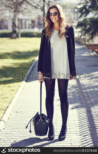 Portrait of beautiful woman smiling, wearing casual clothes, bag and sunglasses in urban background