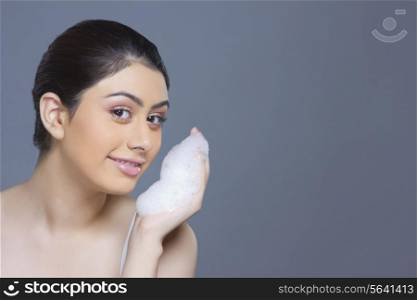 Portrait of beautiful woman washing face with soap sud against blue background