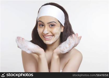 Portrait of beautiful woman washing face with soap sud against white background
