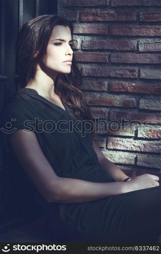 Portrait of beautiful woman wearing casual clothes sitting near a bricks&rsquo; wall