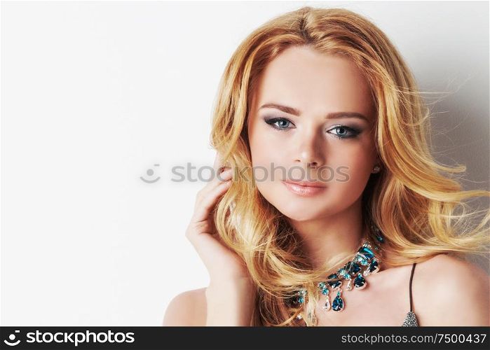 Portrait of beautiful woman with blonde curly hair and necklace of blue precious stones close up. Woman with blonde curly hair and necklace