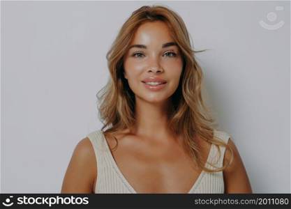 Portrait of beautiful woman with fair hair healthy skin minimal makeup looks tenderly at camera smiles gently dressed in casual t shirt poses against grey background. Natural beauty and feminine. Portrait of beautiful woman with fair hair healthy skin minimal makeup