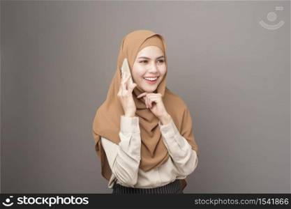 Portrait of beautiful woman with hijab using cellphone on gray background
