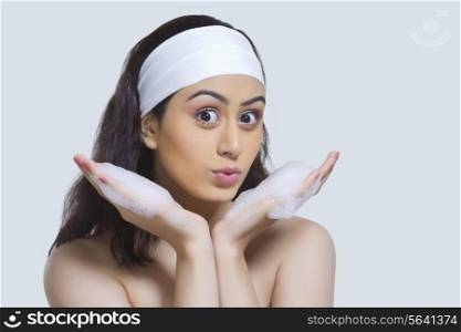 Portrait of beautiful woman with soap sud pouting against gray background
