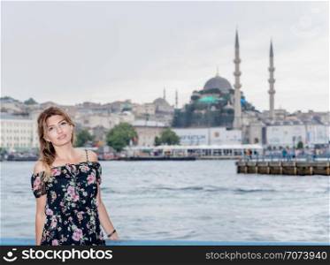 Portrait of beautiful woman with view of Galata bridge,New Mosque and Eminonu Town in Istanbul,Turkey. Beautiful woman travels with ferry between Asia and Europe
