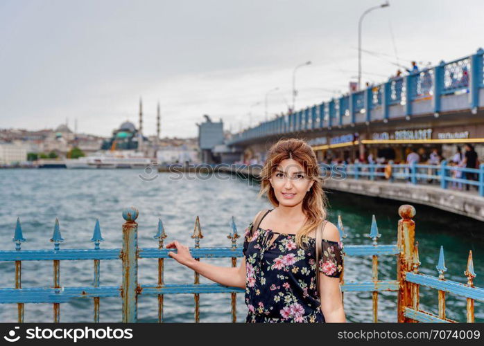 Portrait of beautiful woman with view of Galata bridge,New Mosque and Eminonu Town in Istanbul,Turkey. Beautiful woman travels with ferry between Asia and Europe