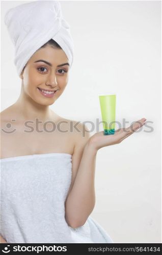 Portrait of beautiful woman wrapped in towel showing beauty product against white background