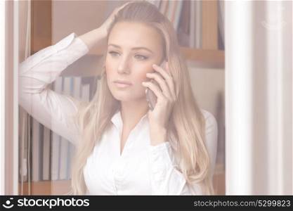 Portrait of beautiful worried business woman standing near windows in the office and discussing some problems on the phone