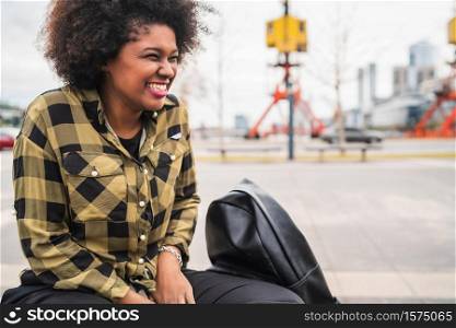 Portrait of beautiful young afro american latin woman with curly hair sitting outdoors in the street.