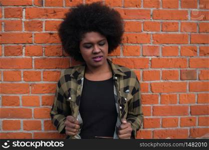 Portrait of beautiful young afro american latin woman with curly hair standing against brick wall.
