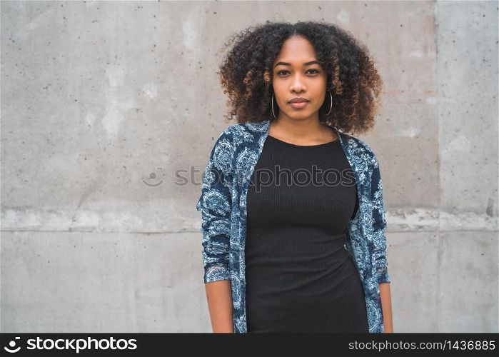 Portrait of beautiful young afro-american woman with curly hair against grey wall.