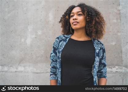 Portrait of beautiful young afro-american woman with curly hair against grey wall.