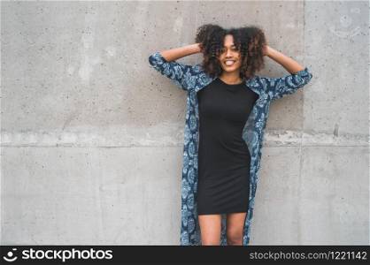 Portrait of beautiful young afro-american woman with curly hair laughing against grey wall.