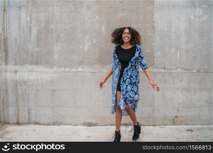 Portrait of beautiful young afro-american woman with curly hair laughing against grey wall.