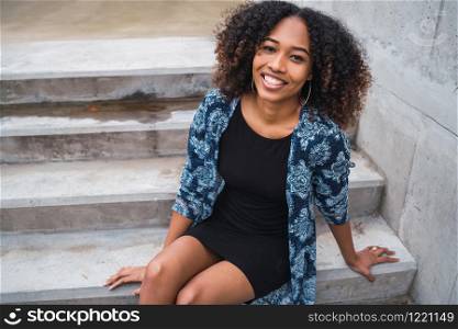 Portrait of beautiful young afro-american woman with curly hair sitting on concrete steps outdoors.