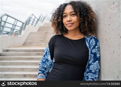Portrait of beautiful young afro-american woman with curly hair standing against concrete stairs outdoors.